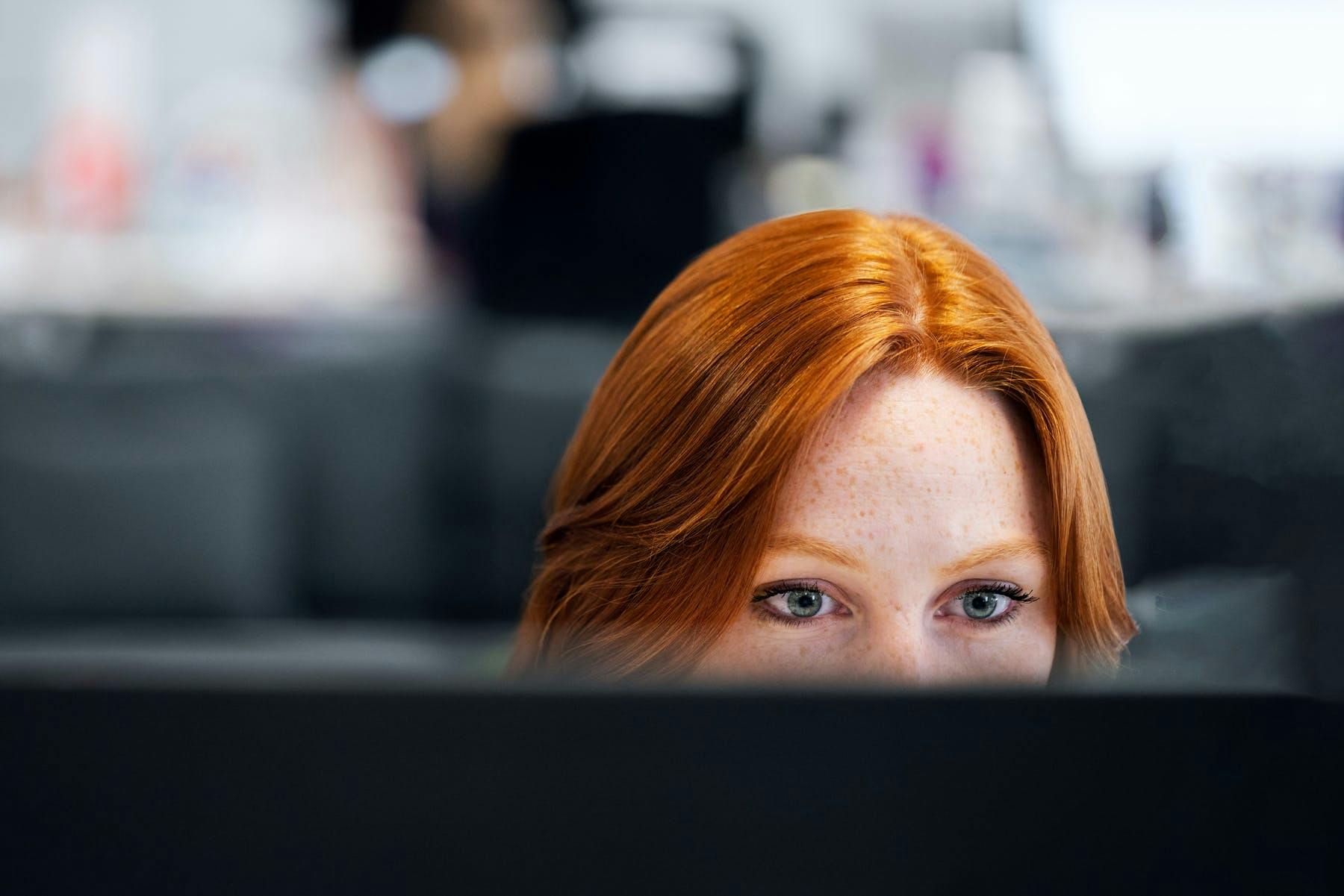 A young redhead female developer close-up focused at a computer screen.