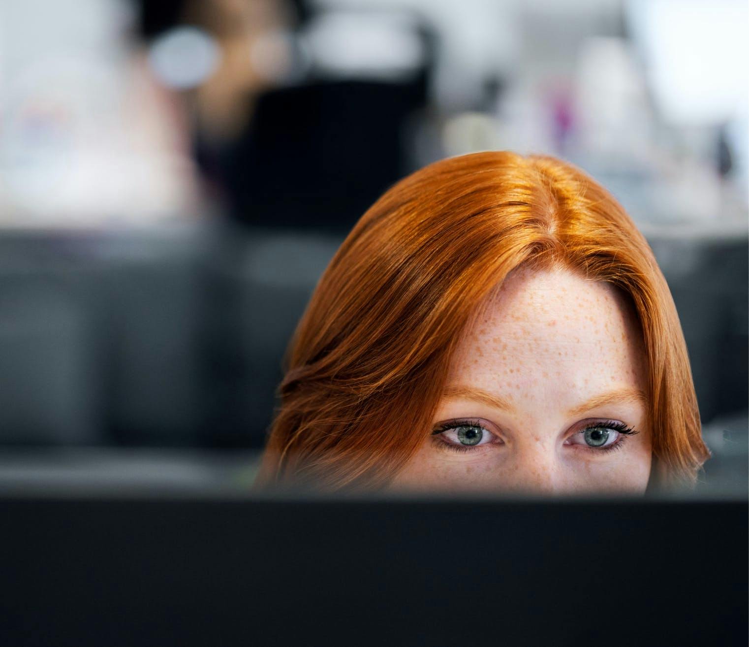 A young redhead female developer close-up focused at a computer screen.